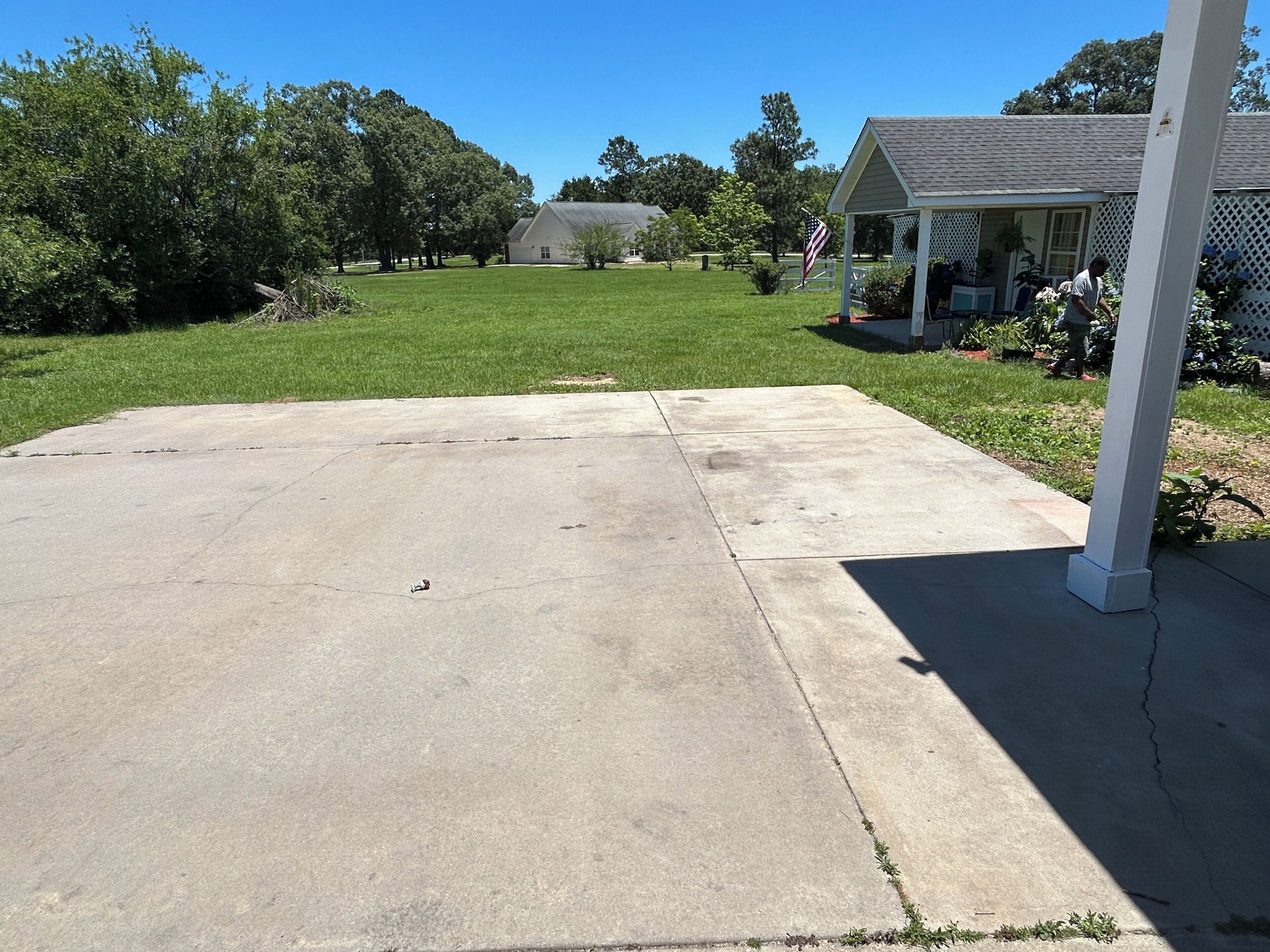 A concrete patio with a white fence, a small porch, and a house in the background.