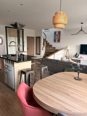 Eine moderne Küche mit Kochinsel, einem Essbereich mit rundem Tisch und einer Treppe, die in einen Wohnbereich führt.