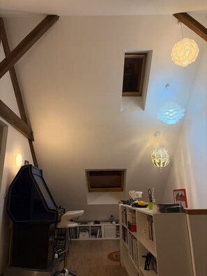 Ein Loft-Zimmer mit freiliegenden Holzbalken, einem eingebauten Grill, einem weißen Schreibtisch, einem Bücherregal und einem Kronleuchter mit Globus.