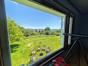Ein Zimmer mit großem Fenster mit Blick auf eine grüne Außenanlage mit Stühlen und einer Feuerstelle.