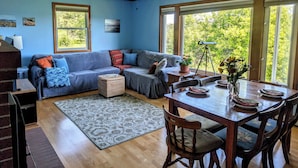 A room with a blue wall, a ceiling fan, a sofa, a dining table with chairs, and large windows.