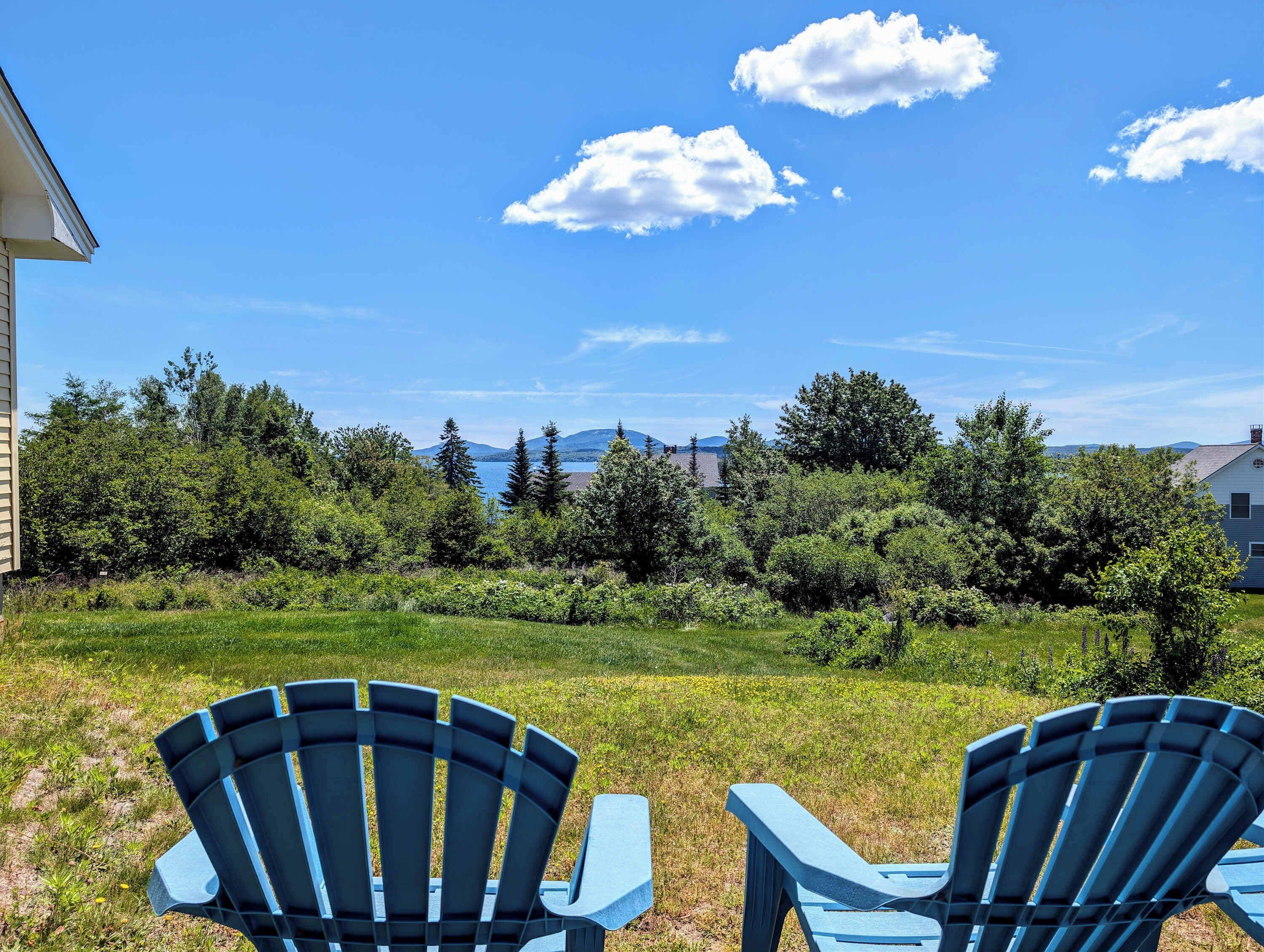 Un patio trasero con dos sillas Adirondack azules, un césped y vistas a árboles y montañas a lo lejos.