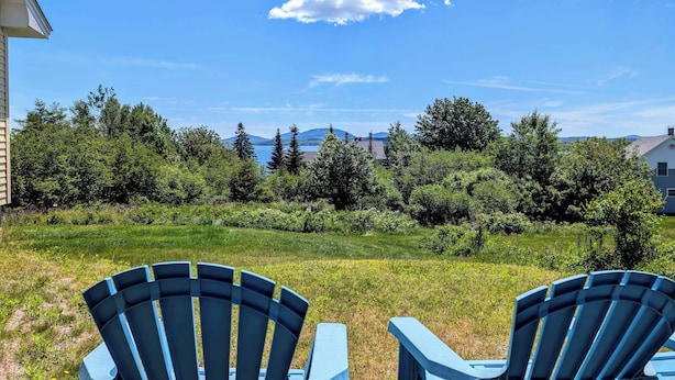 Un patio trasero con dos sillas Adirondack azules, un césped y vistas a árboles y montañas a lo lejos.