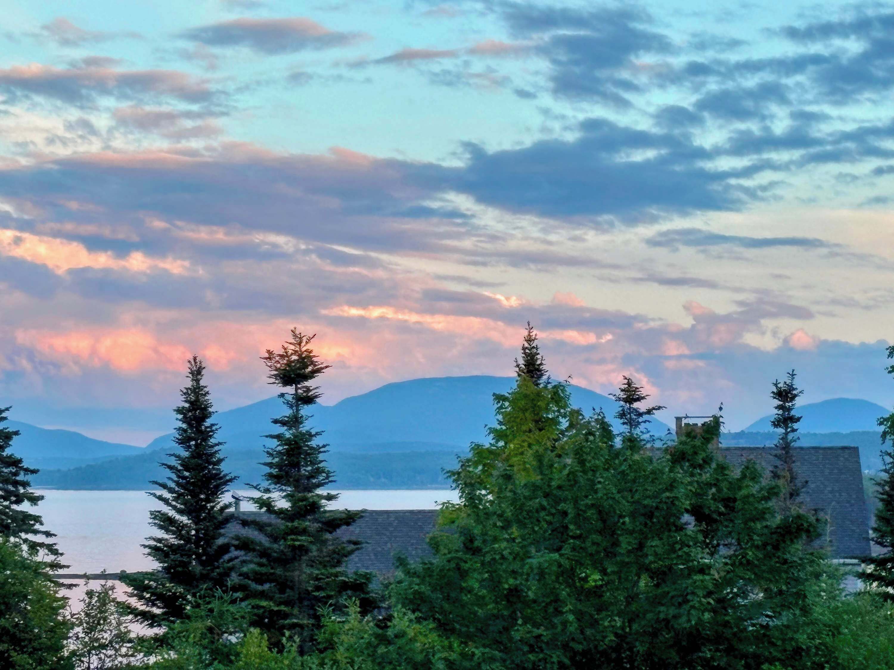 Un paysage montagneux avec un lac, des arbres et un bâtiment doté d’un toit en pente.