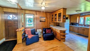 A cozy living room with a sofa, a small table, and a kitchen area with wooden cabinets and a window.
