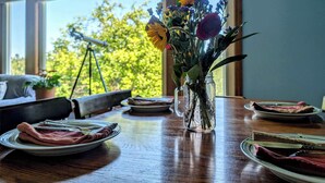 Una mesa de comedor con platos, un jarrón de flores y vistas a árboles a través de amplios ventanales.