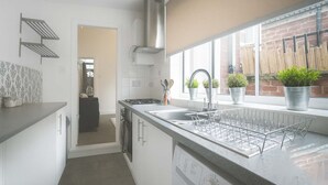 Eine moderne Küche mit weißen Schränken, einer Edelstahl-Dunstabzugshaube, einem eingebauten Geschirrspüler und einem Fenster mit Blumentöpfen.