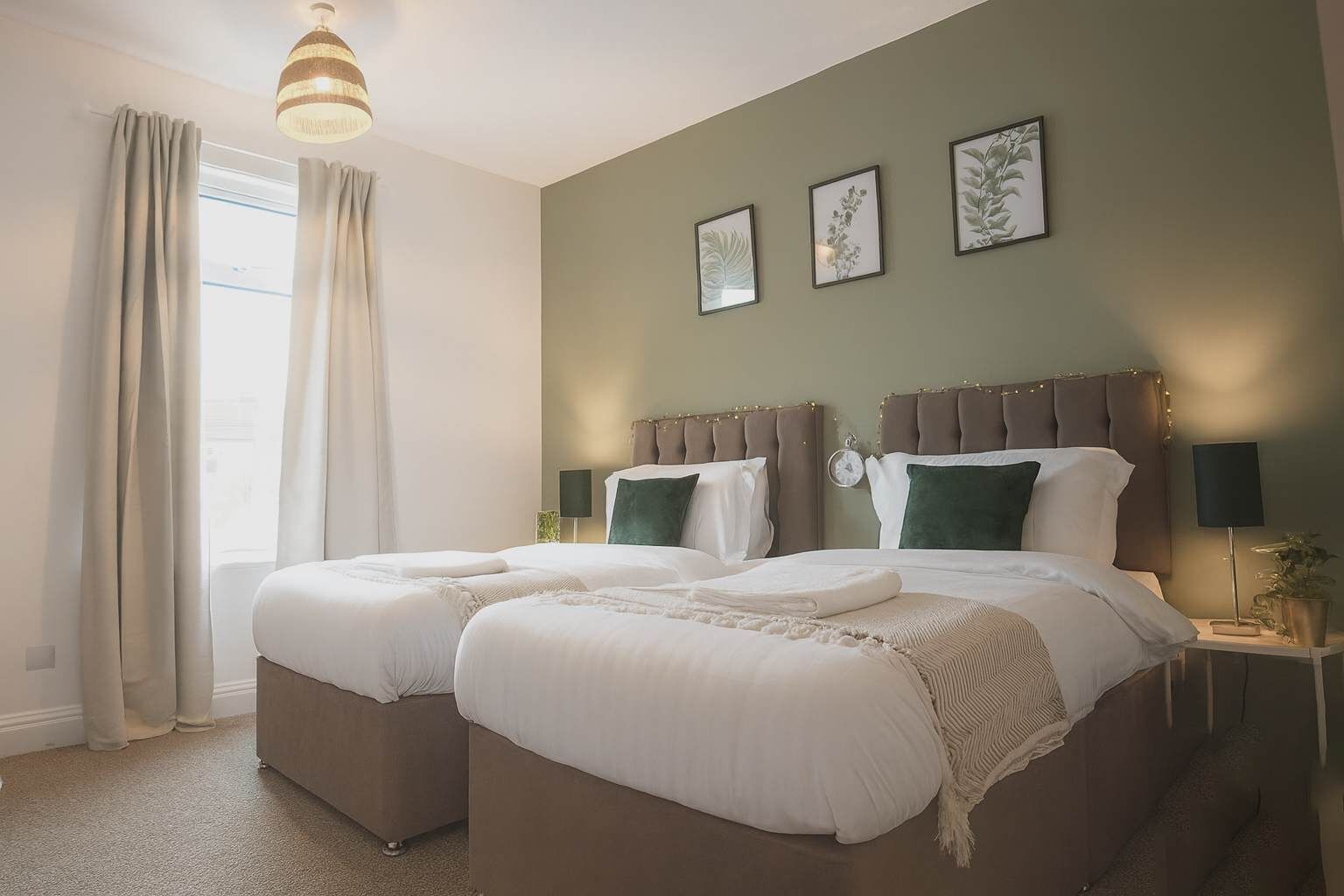 Un lit double avec une tête de lit, deux tables de chevet, une fenêtre avec des rideaux et des œuvres d’art accrochées au mur.