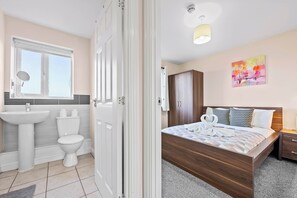 Hotellihuone, jossa on puinen sänky, kylpyhuone, jossa on pesuallas ja wc, sekä taulu seinällä.
