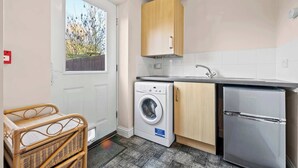Een kleine keuken met een wasmachine, een koelkast en een houten kastje.