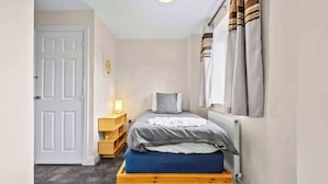 Een slaapkamer met een bed, nachtkastje, lamp, deur en raam met gordijnen.