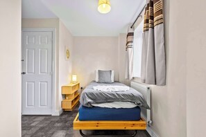 Ein kleines Schlafzimmer mit einem Bett, einem Nachttisch, einer Lampe, einer Tür und einem Fenster mit Vorhängen.