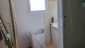 Ett badrum med dusch, ett fönster, en hängande lampa, en vit papperskorg och en trästege.