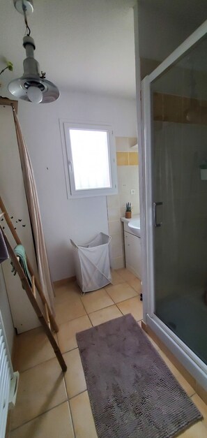 Ein Badezimmer mit Dusche, einem Fenster, einer Pendelleuchte, einer weißen Mülltonne und einer Holzleiter.