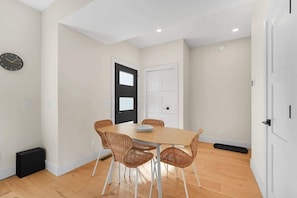 A dining area with a wooden table and wicker chairs, a black door, and a white wall clock. - Modern TC Townhome w/ Rooftop Deck + E-Bikes (Traverse City)