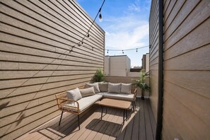 Um deck de madeira com sofá, poltrona, luzes de cordão e um vaso de planta.