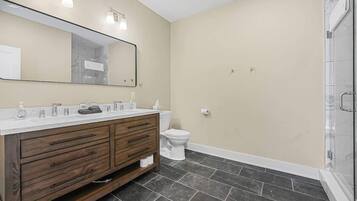 A bathroom with a wooden vanity, a large mirror, a toilet, and a shower area.