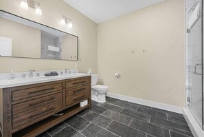 Een badkamer met een houten wastafelmeubel, een grote spiegel, een toilet en een douchehoek.