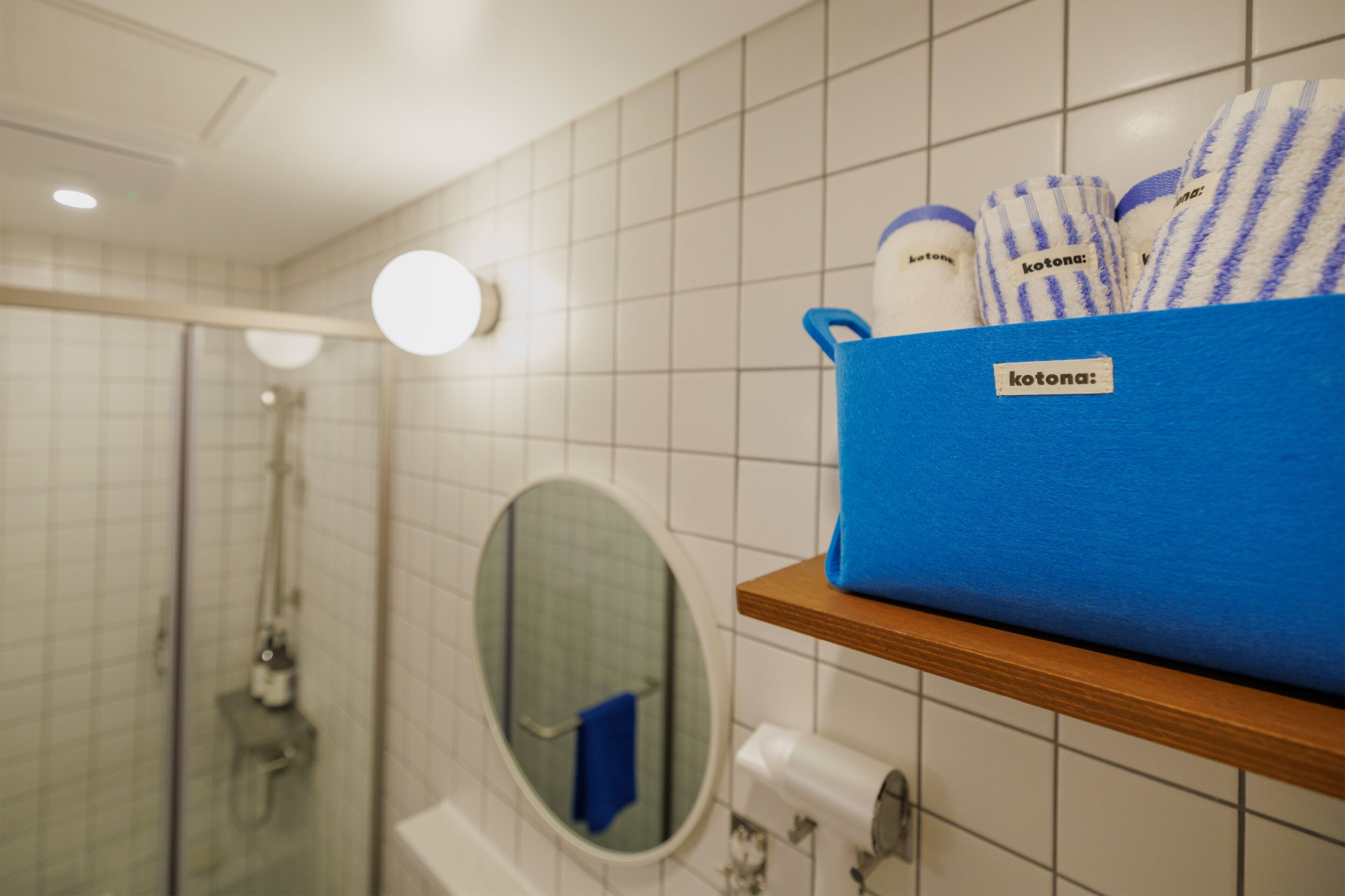 A bathroom with a shower, a mirror, and a blue storage box with towels.