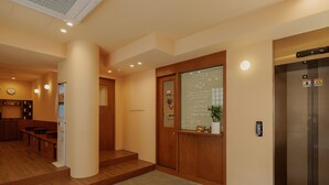 Un área de recepción con un mostrador de madera, una pantalla digital, un reloj y un ascensor.