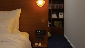 Habitación de hotel con cama, controles junto a la cama, una mesita con un teléfono y una lámpara fijada a la pared.