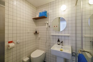 A bathroom with a toilet, sink, mirror, and storage shelves.
