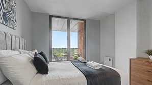 A bedroom with a bed, pillows, a blanket, a wooden dresser, and a balcony with a view. - GuestReady - Chic 2-Bed Apartment with Balcony (Manchester)