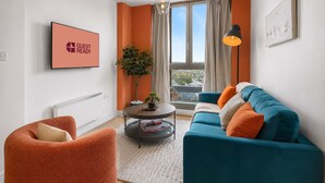 A modern living room with a blue sofa, orange armchair, and a round coffee table. - GuestReady - Chic 2-Bed Apartment with Balcony (Manchester)