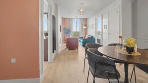 A modern living room with a dining area, a sofa, and a view through a large window. - GuestReady - Chic 2-Bed Apartment with Balcony (Manchester)
