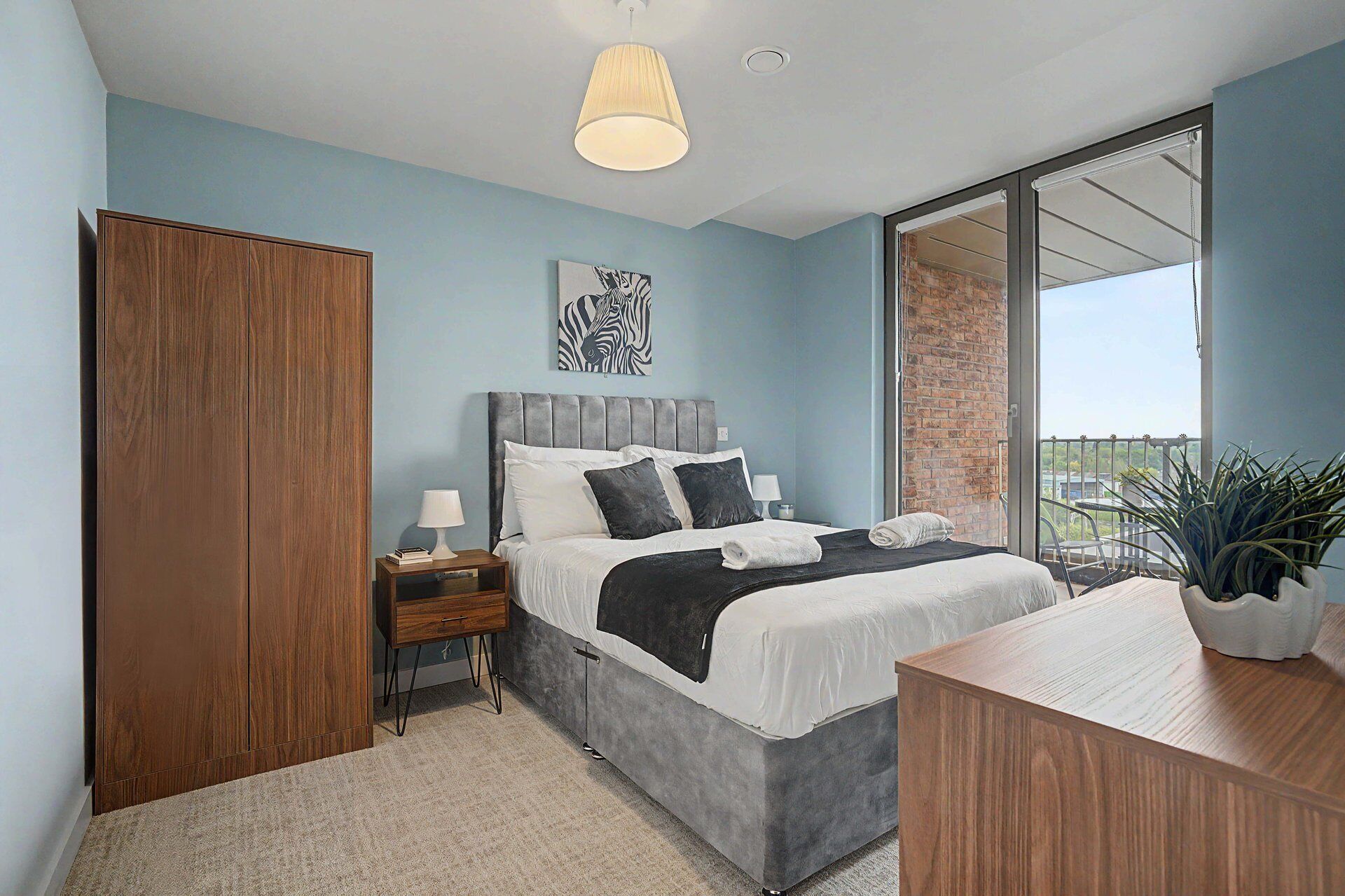 A bedroom with a bed, bedside tables, a wardrobe, a balcony with a view, and a hanging light fixture.