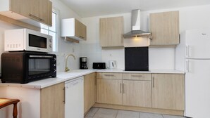 Uma cozinha moderna com armários brancos, micro-ondas, cafeteira e máquina de lavar loiça.