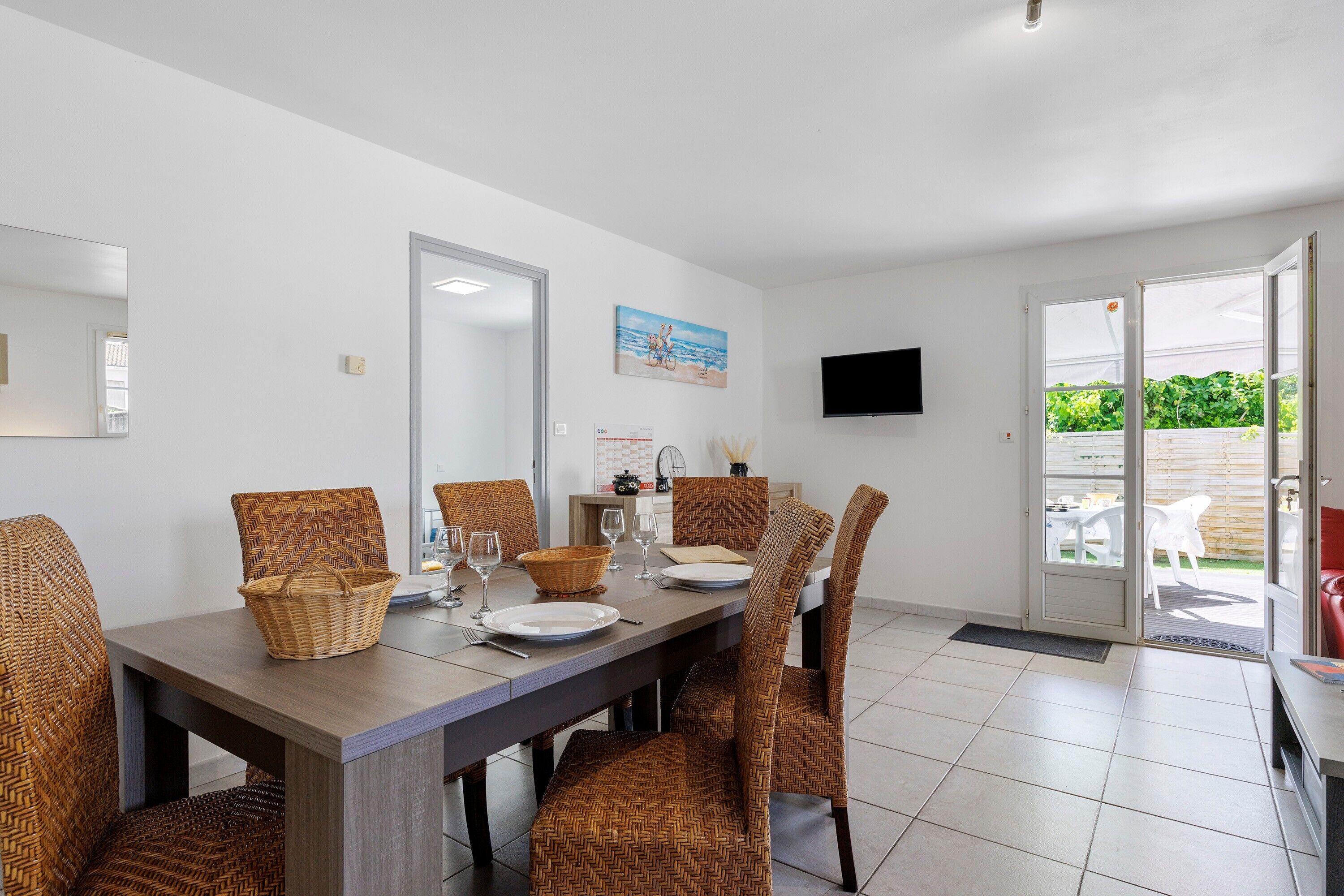 Comedor con sillas de mimbre, una mesa preparada para cuatro personas y un televisor montado en la pared.