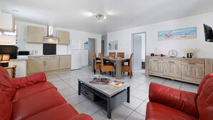 Uma cozinha moderna com armários de madeira, um espaço de refeições com mesa e cadeiras, e uma sala de estar com um sofá vermelho e uma mesa de centro.
