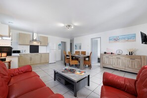 Eine moderne Küche mit Holzschränken, ein Essbereich mit Tisch und Stühlen sowie ein Wohnbereich mit einem roten Sofa und einem Couchtisch.