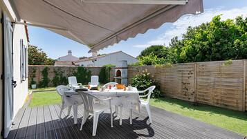 Un portico coperto con tavolo e sedie, un'area con decking in legno e un giardino.