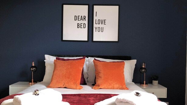 A bedroom with a bed, two pillows, two bedside tables, two framed pictures, and two towels. - Stylish 2BR House in Coventry - Ideal for Business and Groups (West Midlands)