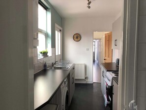 Eine Küche mit eingebautem Geschirrspüler, einer Wanduhr und Blick in den Essbereich.