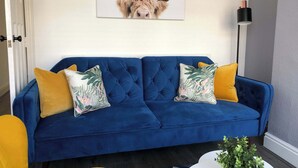 A blue sofa with floral and solid yellow cushions, a wall-mounted animal print artwork, and a floor lamp. - Stylish 2BR House in Coventry - Ideal for Business and Groups (West Midlands)