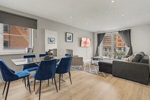 A modern living room with a dining area, a grey sofa, blue chairs, and a TV. - GuestReady - Chic 2bed with Balcony in Liverpool (Liverpool)