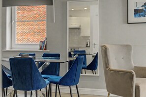 A modern dining area with a glass table, blue chairs, and a beige armchair. - GuestReady - Chic 2bed with Balcony in Liverpool (Liverpool)