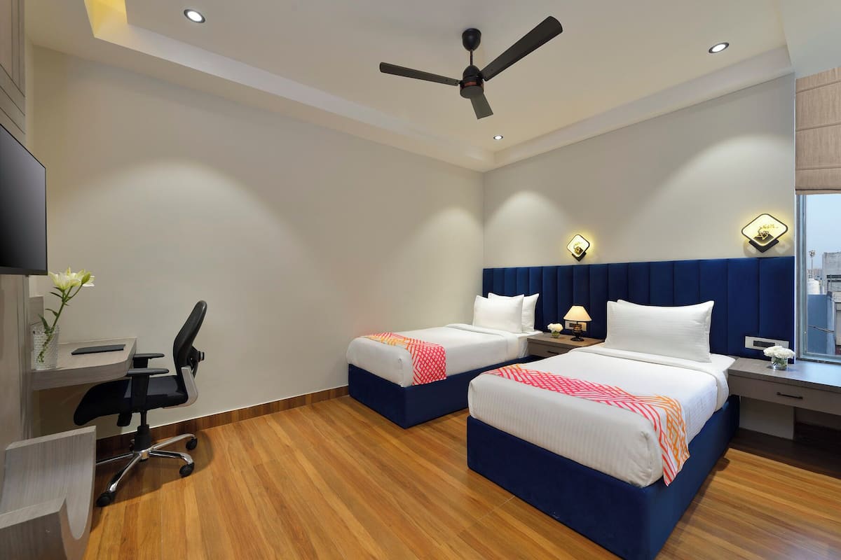 A hotel room with two beds, a desk, a chair, a ceiling fan, and a window.
