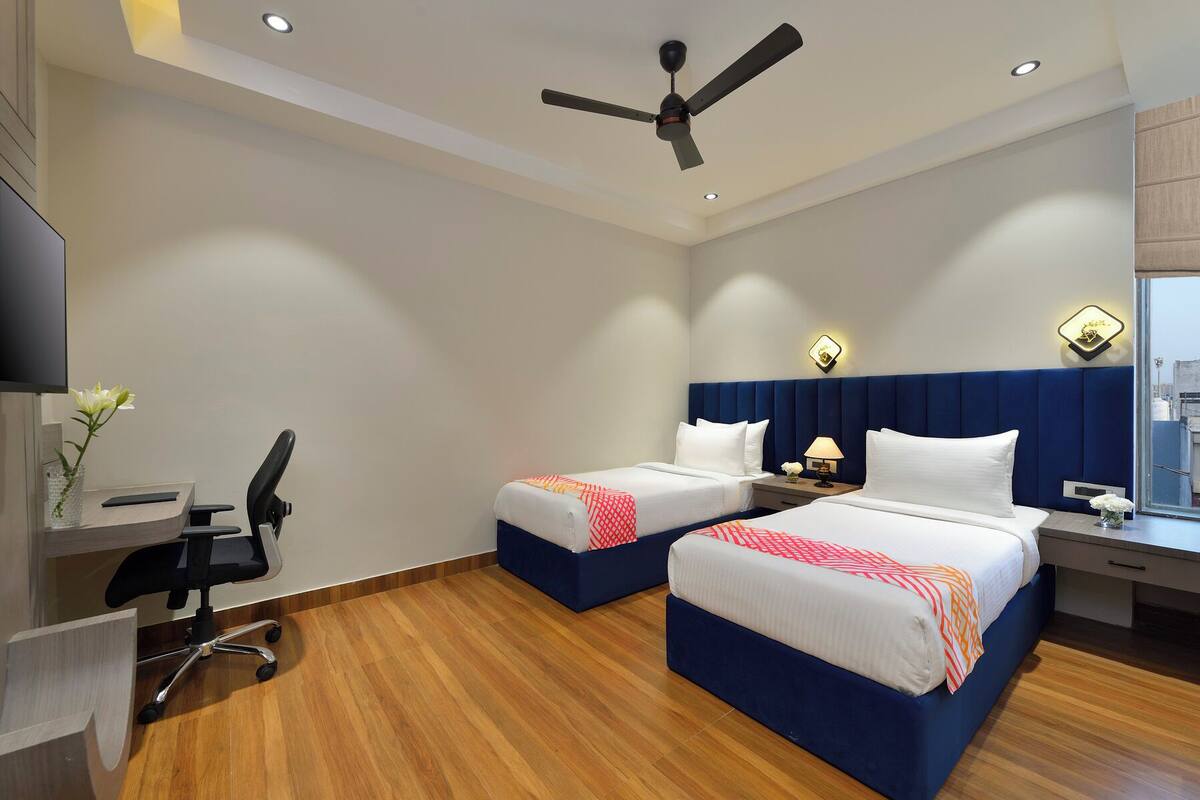 A hotel room with two beds, a desk, a chair, a ceiling fan, and a window.