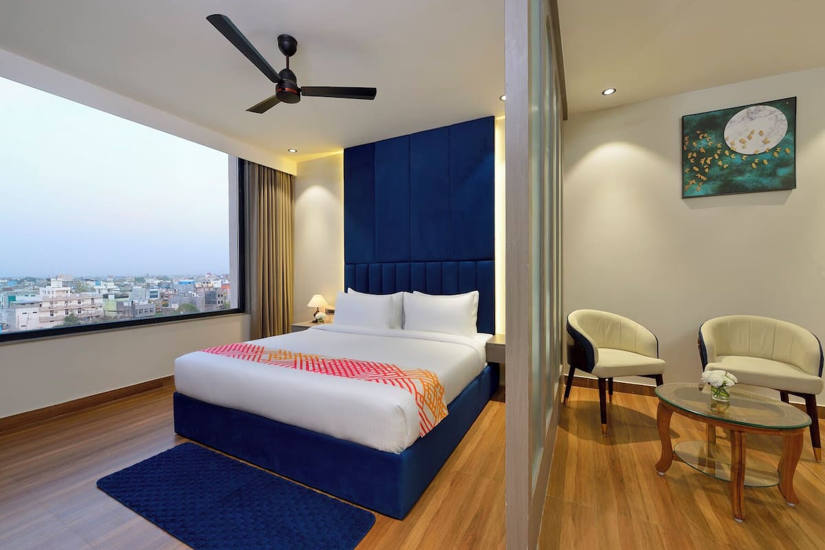 A hotel room with a bed, a ceiling fan, a city view, two chairs, and a small table.
