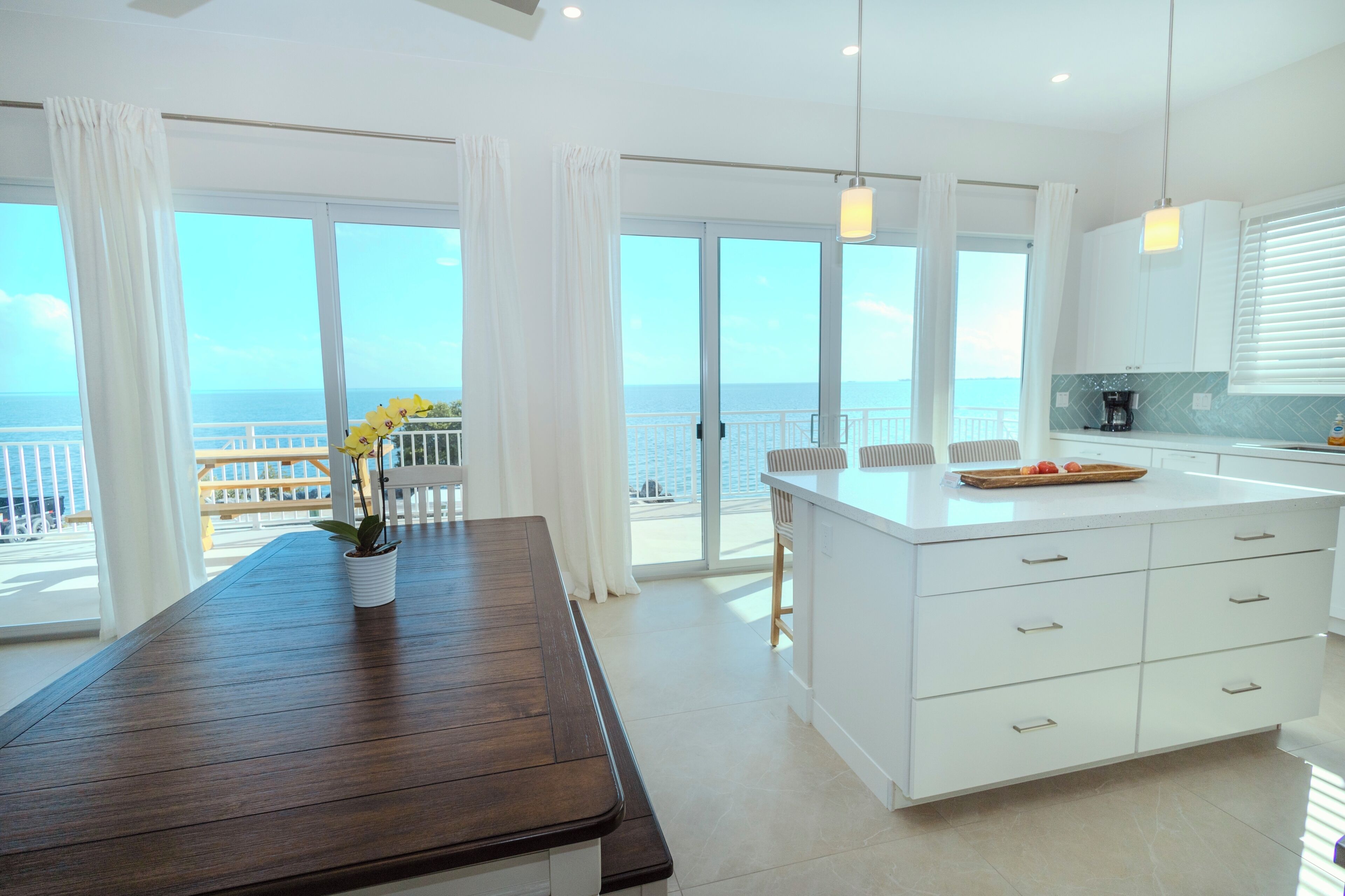 A modern kitchen with a large island, white cabinetry, and a view of the sea.