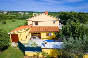 Ein zweistöckiges gelbes Haus mit rotem Ziegeldach, einer kleinen Veranda und einem Garten.