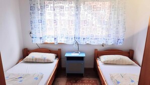 Una habitación pequeña con dos camas individuales, una mesita de noche, un escritorio y una cortina estampada.