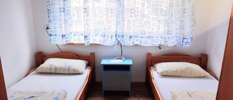 A room with two single beds, a small table, and a window with patterned curtains.