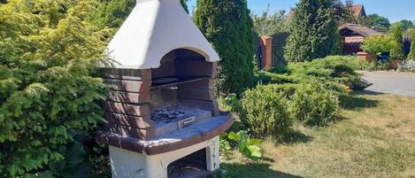 A brick-built outdoor oven with a chimney, surrounded by greenery and a residential area.