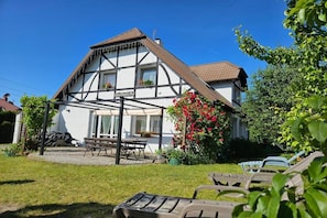Een tweelaags huis met een balkon, een tuin vol bloemen en tuinmeubilair.