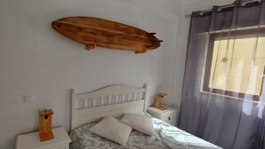 Ein Schlafzimmer mit einem Bett, Nachttischen, einem Holzregal und einem Fenster mit Vorhängen.